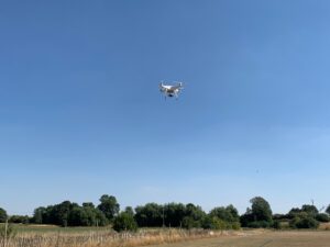 A white drone flying in the sky over a field.